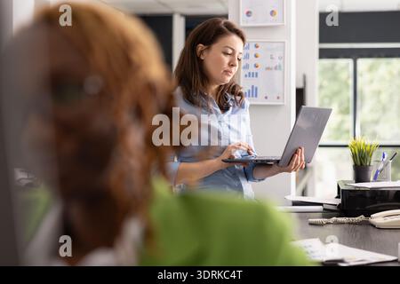Corporate marketing specialist examines company report and analyzes business information on laptop. Professional white woman focuses on planning upcoming work and projects in multinational company. Stock Photo