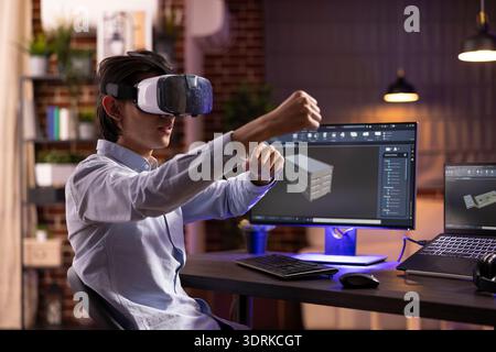 Freelancer with VR headset, developing and modifying 3D product models using cad software at home. Asian man interacts with virtual design projects, combining creativity and futuristic technology Stock Photo