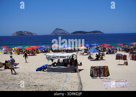 A beach kiosk serves customers on the crowded sands of Ipanema with the Cagarras Islands visible on the background. Stock Photo