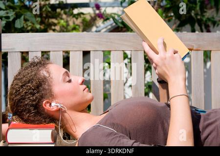 Young woman sits on a bench and reads a book Stock Photo