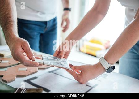 Two hands of individuals, one male and one female, are collaborating on a home renovation project, examining tiles and design pl Stock Photo