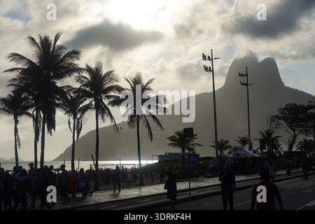 A dramatic silhouette of palm trees and the iconic Morro Dois Irmãos (Two Brothers Mountain) against a bright, hazy sky at Ipanema Beach Stock Photo