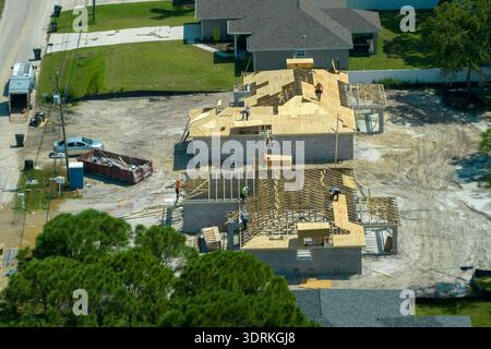 Aerial view of builders working on unfinished residential house with wooden roof frame structure under construction in Florida suburban area Stock Photo