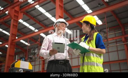Senior engineers and young female workers are talking and inspecting machines on a production line Stock Photo