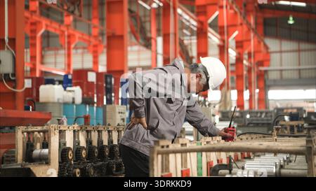 Industrial worker in protective gear experiencing back pain while working on factory machinery Stock Photo