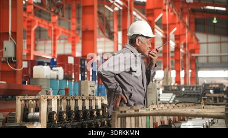Industrial worker in protective gear experiencing back pain while working on factory machinery Stock Photo