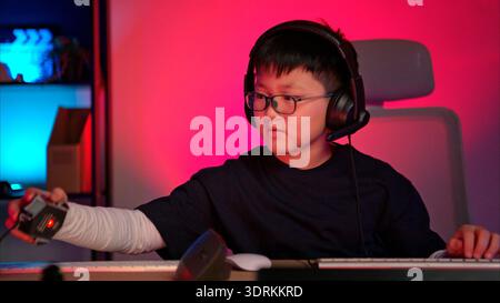 A boy gamer wearing headphones and playing on a desktop computer in a colorful gaming setup Stock Photo