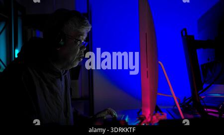 Senior man gamer wearing headphones and playing on a desktop computer in a colorful gaming setup Stock Photo
