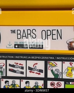 Grammatically incorrect Ryanair onboard advertisement reads "THE BARS OPEN", lacking an apostrophe, displayed above aircraft safety instruction pane Stock Photo