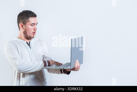 Surprised guy holding and looking at an promotion on laptop screen. Amazed handsome man standing using laptop isolated Stock Photo
