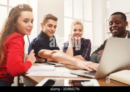 Group of Young People Collaborating in a Workspace While Using a Laptop and Discussing Ideas Stock Photo