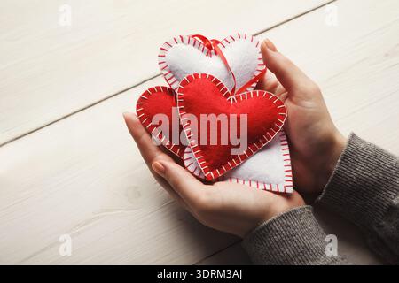 Collection of Handmade Heart Decorations Held in Two Hands on a Wooden Table Stock Photo