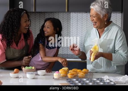 Baking cupcakes together, three generations of African American women sharing laughter. Family, bonding, multigenerational, trad Stock Photo