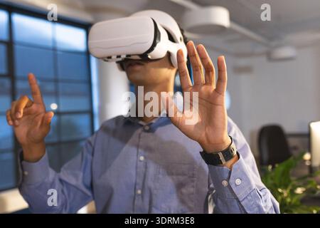 Businessman using VR headset in modern office, interacting with virtual environment. Technology, innovation, virtual reality, di Stock Photo