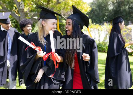 Graduating students outdoors in caps and gowns, holding diplomas and celebrating. Graduation, ceremony, celebration, achievement Stock Photo