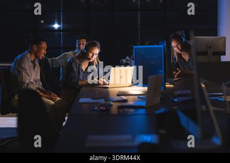 Team collaborating on project at night in modern office, using laptops and headsets. Collaboration, teamwork, technology, brains Stock Photo