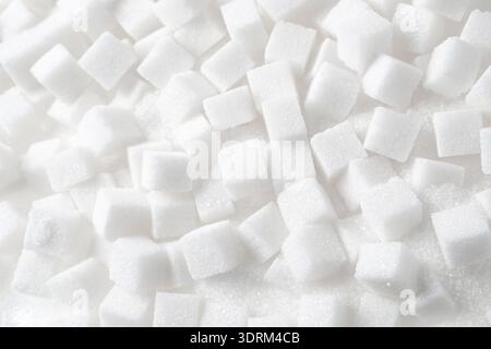 Top view of many white sugar cubes scattered on granulated white sugar. Stock Photo
