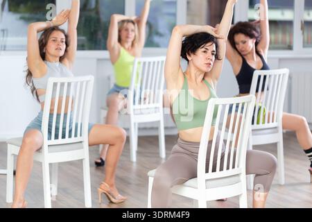 Group of women in high heels rehearsing dance while sitting on chair Stock Photo