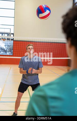 Male volleyball players spiking red white blue ball over net on marked gym court wearing wristband. Athlete, teamwork, active, c Stock Photo