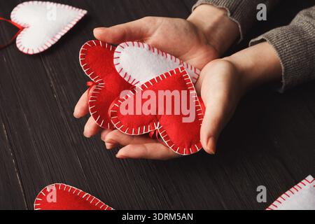 Collection of Handmade Red and White Felt Hearts Held in Hands on a Wooden Table Stock Photo