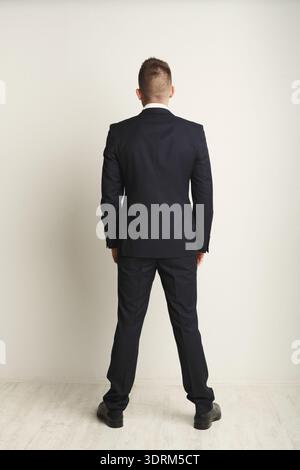 Man in Black Suit Stands Still Facing a Blank Wall in an Indoor Setting While Dressed for an Event Stock Photo