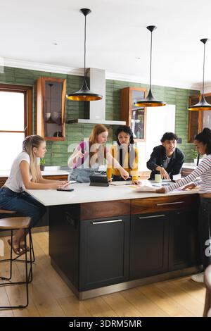 Collaborating on school project, teen friends using tablet and notes in kitchen. Collaboration, teamwork, education, teenagers, Stock Photo