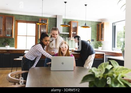 In modern kitchen, teen friends collaborating on laptop, focusing on teamwork. Technology, friendship, collaboration, digital, y Stock Photo