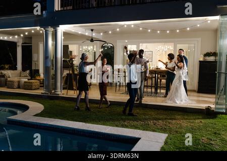 Celebrating joyfully, guests at outdoor wedding reception near pool with string lights. celebration, festive, poolside Stock Photo