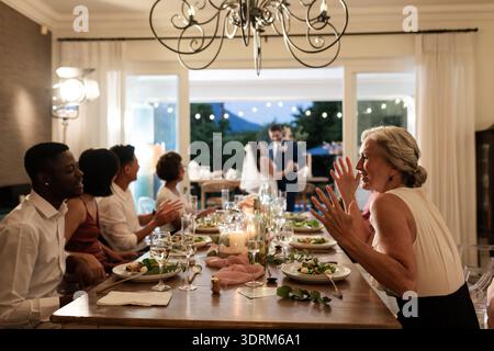 Guests enjoying dinner and conversation while newlyweds dance in background. Wedding, celebration, reception, dancing, hospitali Stock Photo