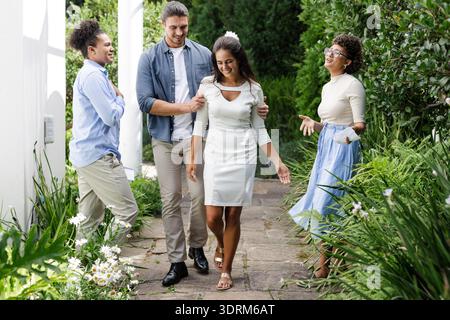 Friends joyfully walking with bride in garden, celebrating wedding day together. Celebration, happiness, love, friendship, cerem Stock Photo