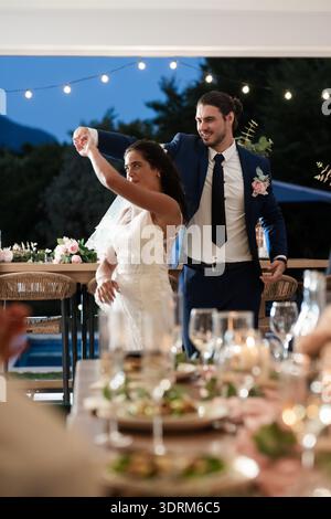 Bride and groom dancing joyfully at outdoor wedding reception under string lights. celebration, romance, outdoors, festivities, Stock Photo