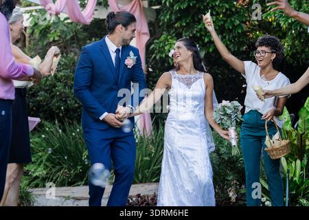 Bride and groom walking joyfully as guests celebrate with bubbles outdoors. Wedding, celebration, marriage, happiness, festive, Stock Photo