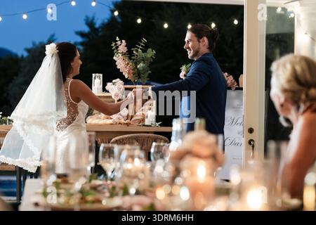 Bride and groom dancing joyfully at outdoor wedding reception under string lights. celebration, happiness, dance, romance, eveni Stock Photo