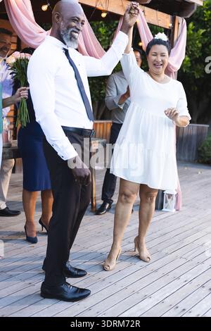 African American couple dancing joyfully at outdoor celebration with friends. party, happiness, friendship, music, fun Stock Photo