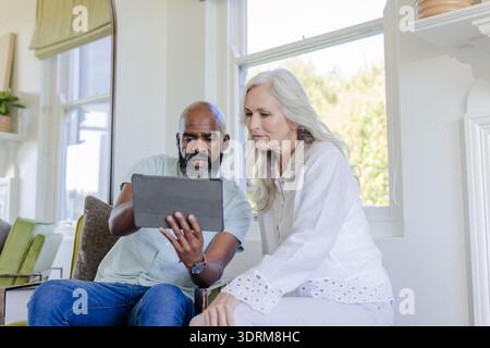 African American man and woman using tablet together at home, looking focused. Technology, collaboration, connection, digital, l Stock Photo