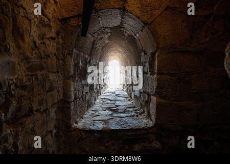 Narrow stone tunnel with vaulted ceiling leading to a bright exit inside a historic fortress in Olivenza, Extremadura, Spain. Stock Photo