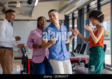Dancing and laughing, colleagues enjoying lively break together in office. Teamwork, collaboration, workplace, cheerful, joyful, Stock Photo