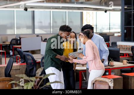 Team collaborating in modern office, excitedly discussing project on digital tablet. Teamwork, collaboration, brainstorming, inn Stock Photo