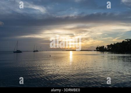 A beautiful sunset over Tahaa Island in French Polynesia, with calm waters and sailboats creating a serene atmosphere Stock Photo