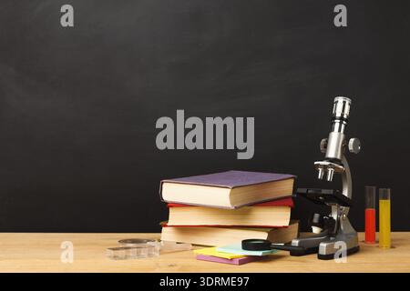 Set of Science Tools and Books Arranged on a Wooden Table Near a Chalkboard Wall Stock Photo