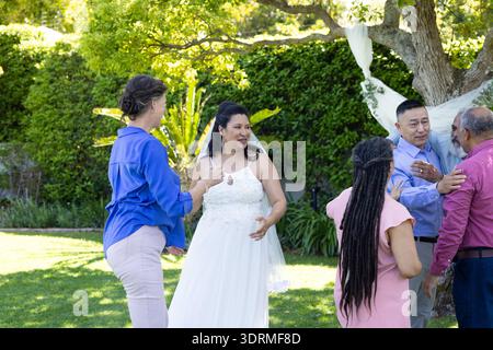Celebrating in lush garden, bride in white dress joyfully with friends. senior wedding, celebration, friendship, happiness, outd Stock Photo