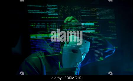 Anonymous hacker wearing a mask and hoodie interacting with digital data in a dark room Stock Photo