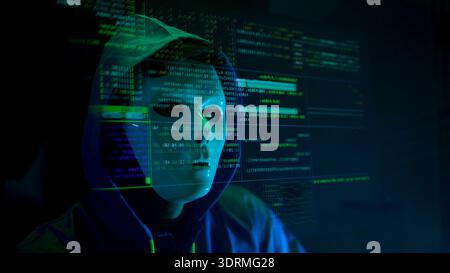 Anonymous hacker wearing a mask and hoodie interacting with digital data in a dark room Stock Photo
