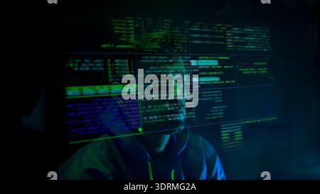 Anonymous hacker wearing a mask and hoodie interacting with digital data in a dark room Stock Photo