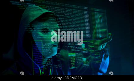 Anonymous hacker wearing a mask and hoodie interacting with digital data in a dark room Stock Photo