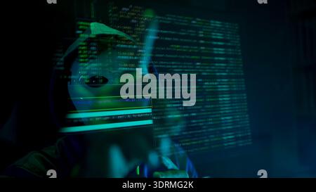 Anonymous hacker wearing a mask and hoodie interacting with digital data in a dark room Stock Photo