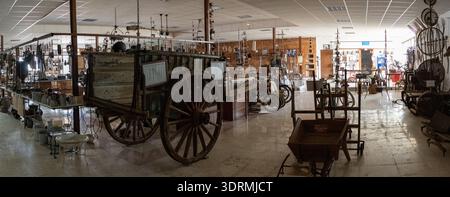 Almodovar del Rio, Spain - 15 Oct 23: Wide panoramic view of an ethnology museum hall featuring wooden carts, hanging tools, and historical objects in Stock Photo