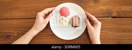 Hands holding plate with colorful macarons on wooden table Stock Photo