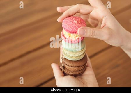 Stack of colorful macarons held by caucasian female on wooden table background Stock Photo