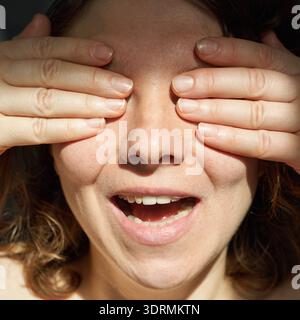 Caucasian young adult female surprised expression with hands covering eyes Stock Photo